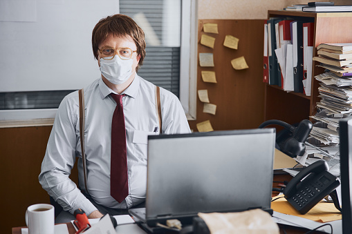 Portrait of a serious adult businessman or employee doing his paperwork in an office protecting face with mask to avoid coronavirus