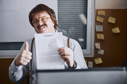 Middle-aged office employee showing camera an important agreement he had reached while his face is lighting up with joy