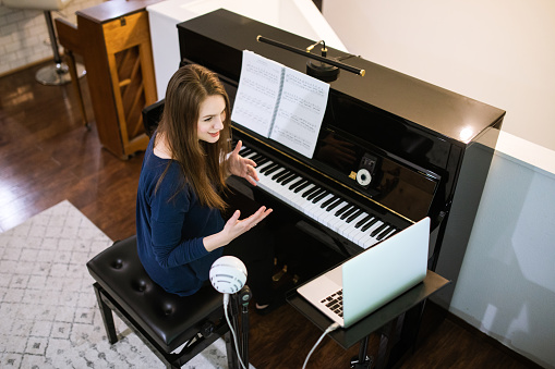 A woman teaches her piano lessons virtually, streaming live with her students on an online platform.  Part of normal video instruction or a necessity during a lockdown global pandemic of Coronavirus.