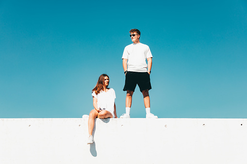 Fashionable Lifestyle Young Couple Modern Urban Portrait. Young man and woman together on top of concrete wall wearing sunglasses. Modern Couple Lifestyle Portrait. Edited Colors.