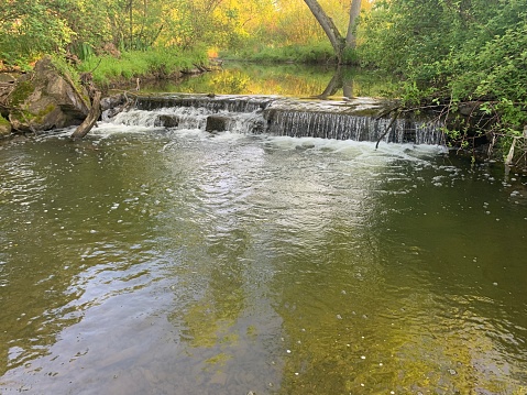 Image of Panoramic shot of a rocky riverbank with water rushing by and green trees in the background