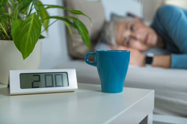 Digital Alarm clock and cup of coffee at night table. Sleepless female suffering from insomnia in the background.