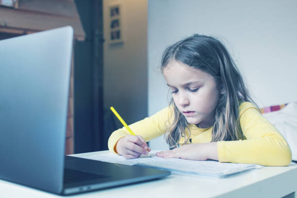 istock Pretty school child, sitting at the table with laptop, writing school tasks while homeschooling 1227046366