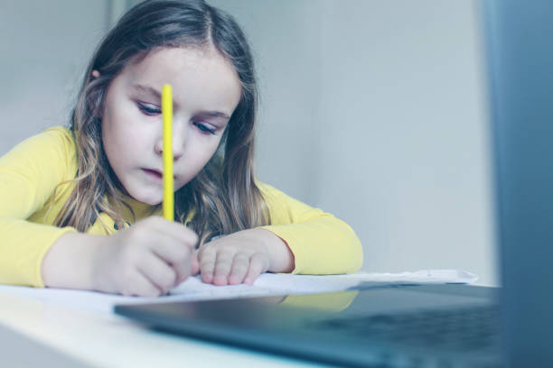 istock Pretty cute schoolgirl studying at home writing and using laptop. 1227046411