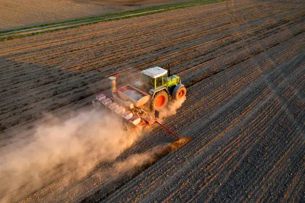 Tractor drilling seed in plowed field, aerial view.