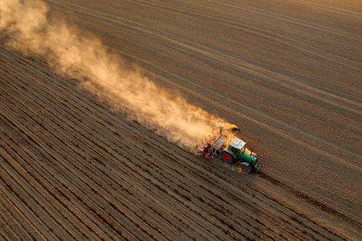 Tractor drilling seed in plowed field, aerial view.