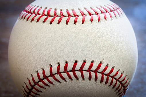 Close-up of an old baseball on a cement floor. Faded red stitching and old worn leather.