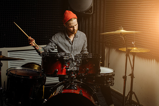young modern caucasian man professionally playing on drums. talented man in red hat play on drums, enjoy music. rock and roll, instruments concept