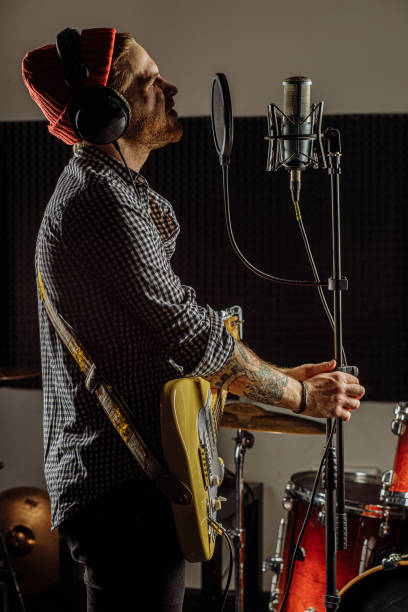 young talented caucasian musician play guitar and sing on microphone, professional guitarist preparing for rock concert in recording studio. music, instruments concept