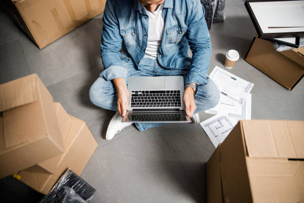 istock Man with laptop and coffee in flat with cardboards 1227054309