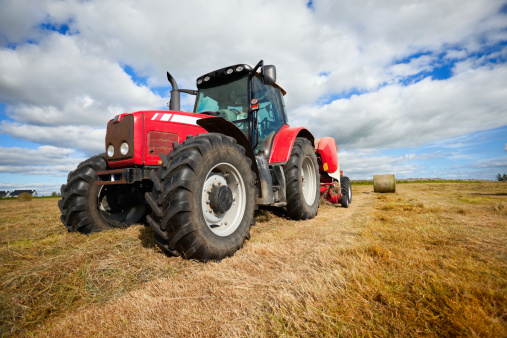 huge tractor collecting haystack in the field in a nice blue sunny day