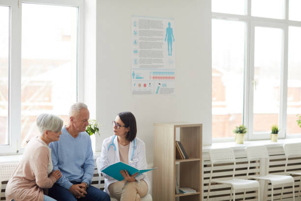 Female Doctor Registering Senior Couple Senior Couple Wide angle portrait of young female doctor talking to senior couple while sitting in reception area of modern clinic, copy space waiting room stock pictures, royalty-free photos & images