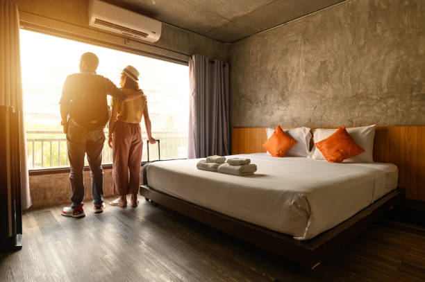 portrait of young couple tourist standing nearly window, looking to beautiful view outside in hotel/resort bedroom after check-in. - estalagem imagens e fotografias de stock