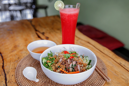 Close up shot of Vietnamese vermicelli noodle ( bun thit nuong ) topped with grilled pork, herbs and vegetables, with fresh strawberry juice on the side