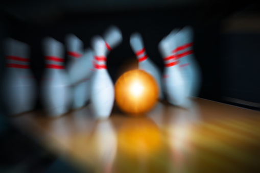 Red bowling ball hitting pins in the bowling alley before blue background. Horizontal composition with copy space. Bowling concept.