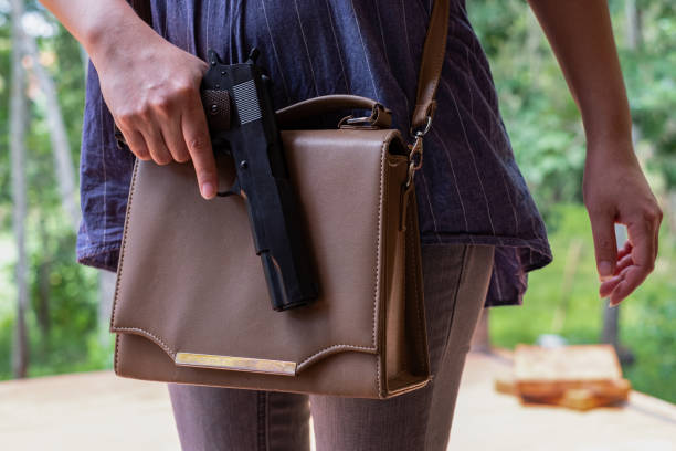 jovem asiática colocando uma arma em sua bolsa, mão de mulher puxando uma pistola para fora do saco no parque - gun women handgun armed forces - fotografias e filmes do acervo