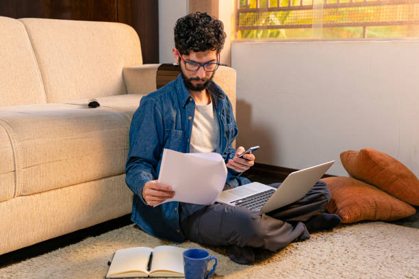 istock Hispanic man checking document and holding cell phone sitting on the floor of his office 1227081136