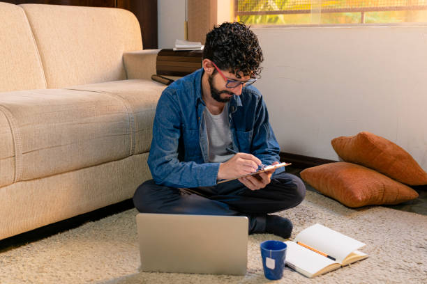 istock Model taking notes sitting on the carpet in her living room. Work at home concept 1227081227