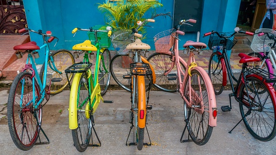A row of bikes painted bright blue, yellow, orange, pink and red, parked next to a curb.