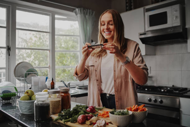 Young woman taking photo of her food with smart phone in modern kitchen at home during isolation and quarantine Young woman taking photo of her food with smart phone in modern kitchen at home - isolation and quarantine camera phone photo stock pictures, royalty-free photos & images
