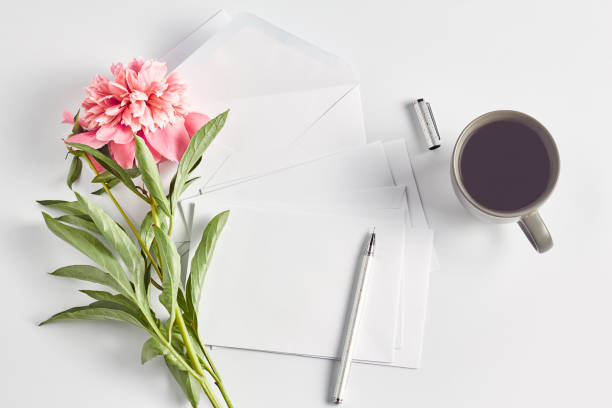 istock female workspace, pink peony flowers, grey coffe mug, white envelope and silver pen. flat lay women 1227086609