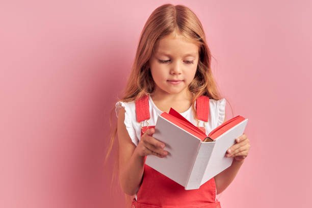 istock Mindful girl attentively read book isolated over pink background 1227087617