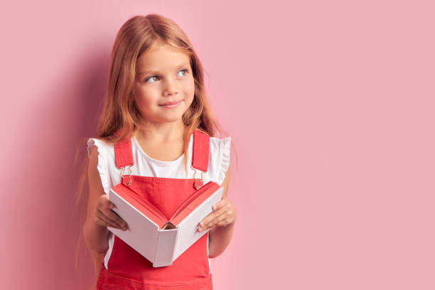 retrato de garota coquetish sonhadora com livro nas mãos isolado sobre fundo rosa - reading girl - fotografias e filmes do acervo