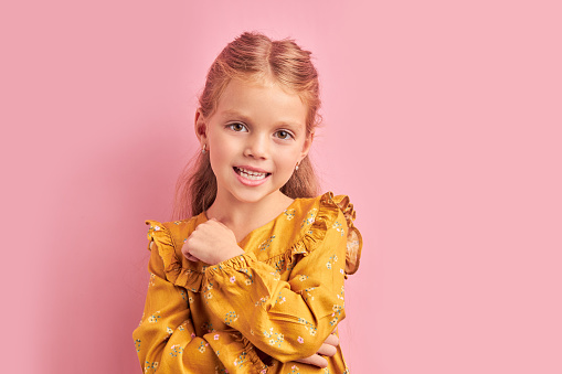 Sweet little girl in yellow dress look at camera posing. Pink isolated background