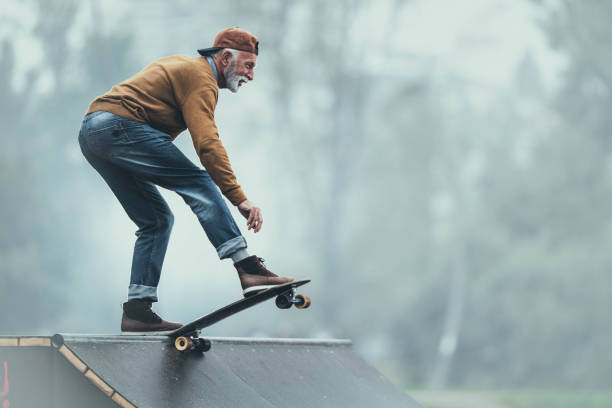 homme aîné heureux faisant du skateboard sur une rampe au stationnement. - skate photos et images de collection