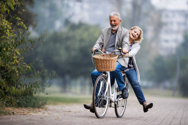 秋の日に自転車で楽しんでいる遊び心のあるシニアカップル。 - retirement mature couple couple bicycle ストックフォトと画像
