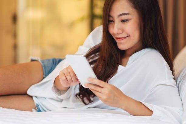 istock a beautiful asian woman using and looking at mobile phone while lying down on a white bed 1227091811