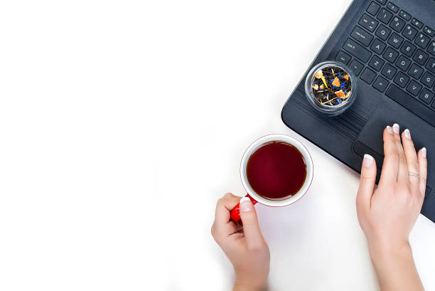 as mãos das mulheres seguram uma xícara de chá trabalhando em um laptop. ervas de chá seco em uma xícara de vidro no fundo branco. - heart shape isolated isolated on white tea leaves - fotografias e filmes do acervo
