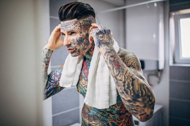 Young Man With Whole Body Covered In Tattoos Looking At His Face In The  Bathroom Mirror Stock Photo - Download Image Now - iStock