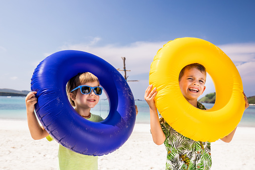 Happy little friends having fun with swimming tubes during summer day on the beach.
