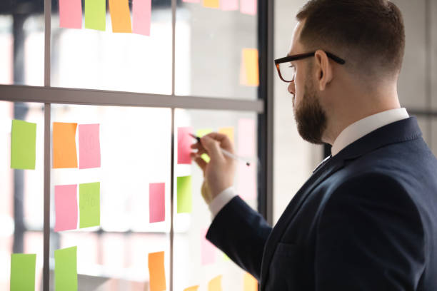 Confident leader wearing glasses writing tasks on sticky papers