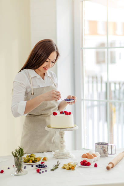 istock smiling girl decorating the surface of cake with different berries 1227095218