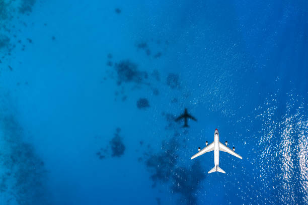 Aerial top down view of an airplane flying over blue sea Aerial top down view of an airplane flying over blue sea as a travel concept with copy space planes flying overhead stock pictures, royalty-free photos & images
