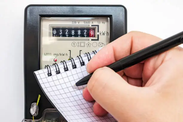 Photo of Man with pen and notepad writes the electrical meter readings. Payment of utility services.