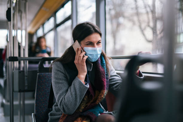 Woman With Protective Mask Talking On The Phone. Woman with protective face mask sitting in city transport and talking on the phone. public transportation photos stock pictures, royalty-free photos & images