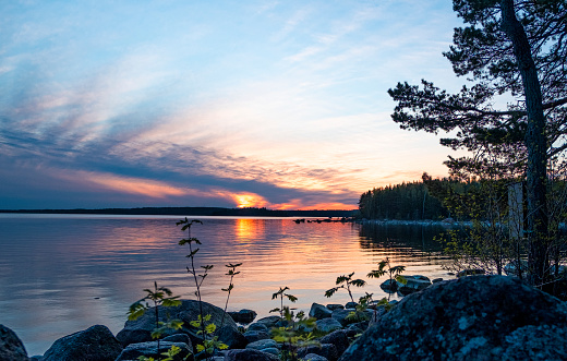Bright, orange, sunset over the sea. The coastline of a rocky shore. Reflection of trees and sun in the water. No windy weather. Finland, Santalahti natural park in the city of Kotka. Travel and eco-tourism in Finland.