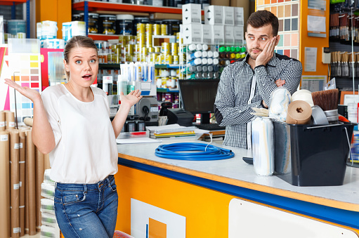 Young diligent   man seller discussing with upset unhappy female customer  in tool-ware shop