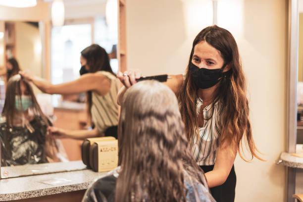 hairdresser with mask enjoying to work again in her hair salon after lockdown is over happy smiling woman hairdresser coiffeur cutting womans long hairs during first weeks of reopening in times of covid-19 crisis again stock pictures, royalty-free photos & images