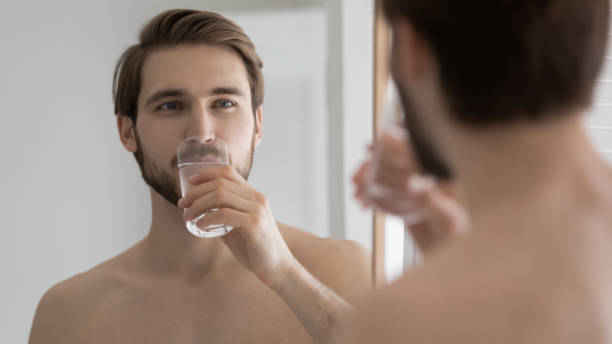istock Young man look in bathroom mirror drinking water 1227112918