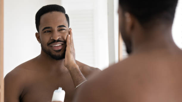 若いアフリカ系アメリカ人男性は、バスルームで顔のクリームを適用します - men naked shower bathroom ストックフォトと画像
