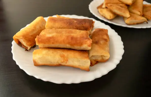 Photo of Vegetable spring rolls and mini samosa on dark wooden background.
