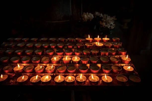 Closeup of votive candles, tea lights, in a dark Christian church. Italy, Europe