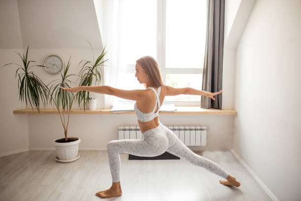 istock Woman practicing Warrior yoga pose indoors against window background 1227132391