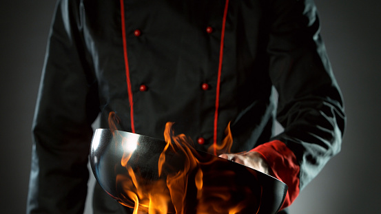 Closeup of chef holding empty wok pan in fire, ready to prepare for cooking.