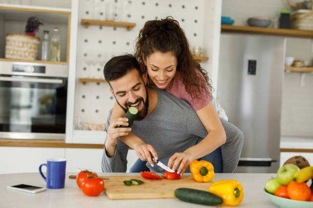 istock Playful couple preparing salad in a domestic kitchen 1227134120