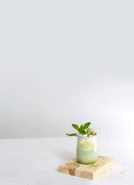 Healthy matcha dessert with aquafaba. Glass jar on wooden board on neutral background with copy space. Vertical. Green matcha for vegetarians. Weight loss concept, gluten free, sugar free dessert